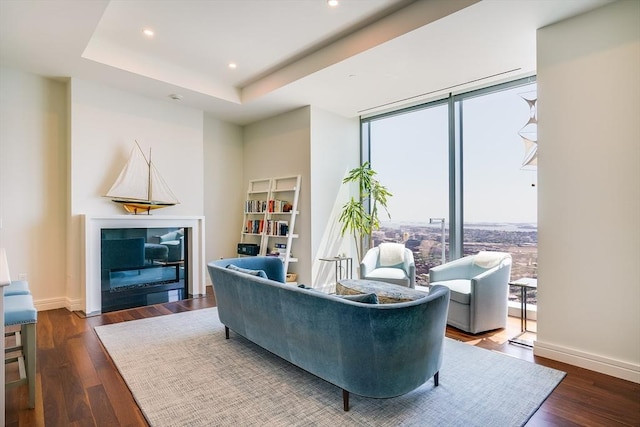 living room featuring a tray ceiling, built in shelves, and dark hardwood / wood-style flooring