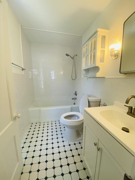 full bathroom with tiled shower / bath combo, tasteful backsplash, toilet, vanity, and tile walls