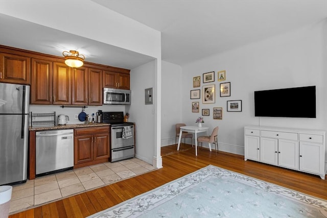kitchen with light wood-type flooring, baseboards, brown cabinets, and appliances with stainless steel finishes