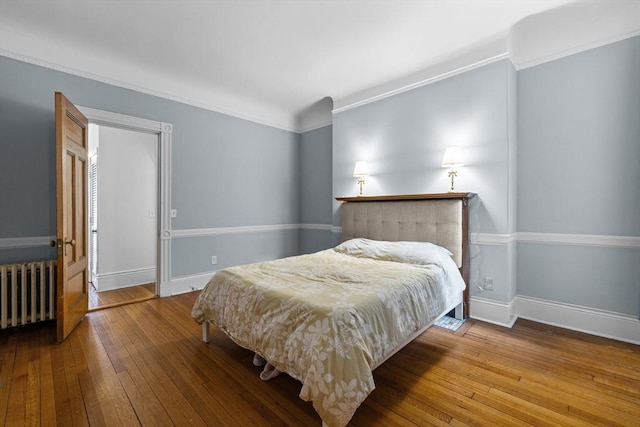 bedroom featuring radiator heating unit, hardwood / wood-style floors, crown molding, and baseboards