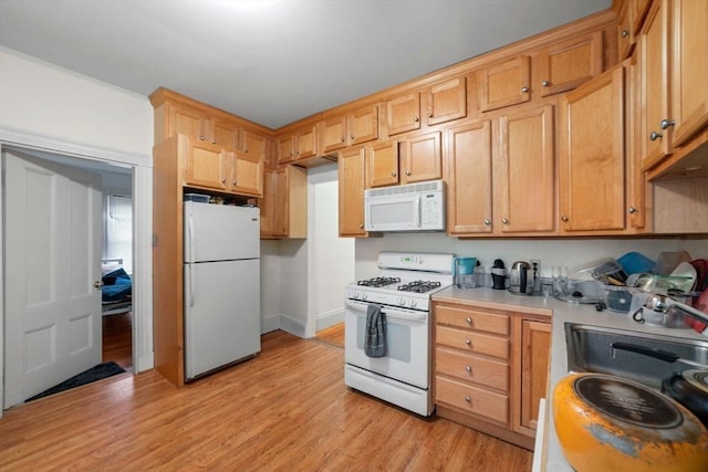 kitchen featuring light wood finished floors, light countertops, a sink, white appliances, and baseboards