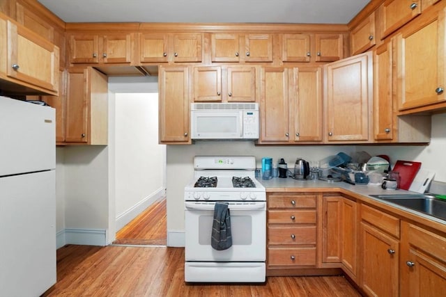 kitchen featuring light wood finished floors, light countertops, a sink, white appliances, and baseboards