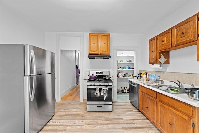 kitchen with under cabinet range hood, stainless steel appliances, a sink, light countertops, and light wood-type flooring