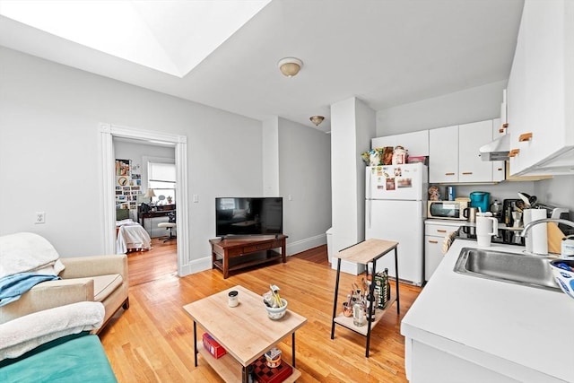 living area featuring a skylight, light wood-style flooring, and baseboards