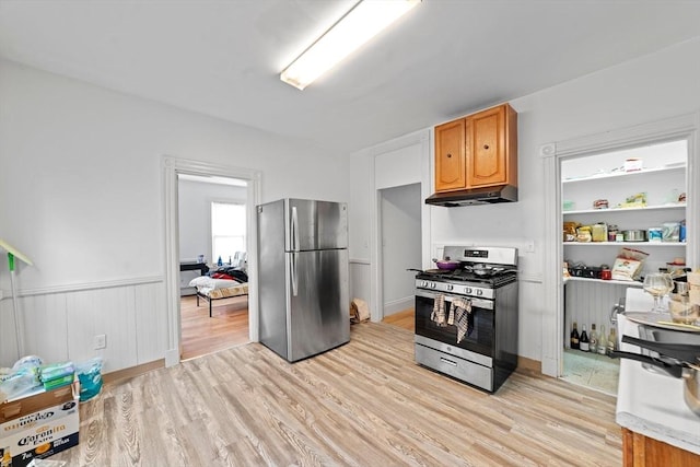 kitchen with light wood-type flooring, under cabinet range hood, appliances with stainless steel finishes, and wainscoting