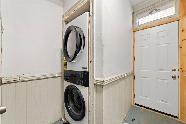 laundry area with stacked washer and clothes dryer, a wainscoted wall, wood walls, and laundry area