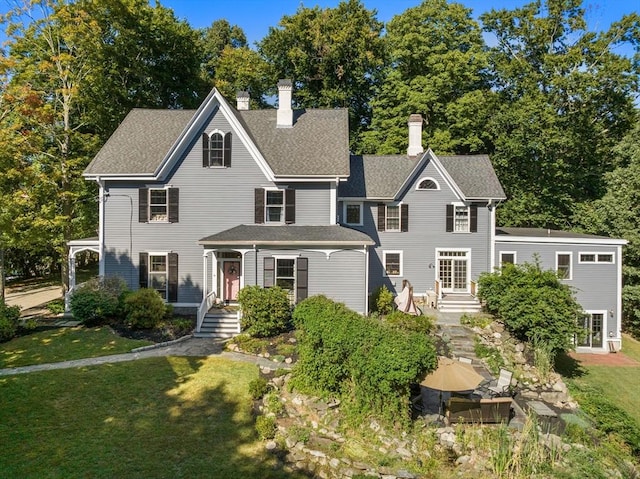 view of front of property with a shingled roof, a chimney, and a front yard