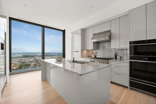 kitchen with expansive windows, decorative backsplash, a sink, modern cabinets, and wall chimney exhaust hood
