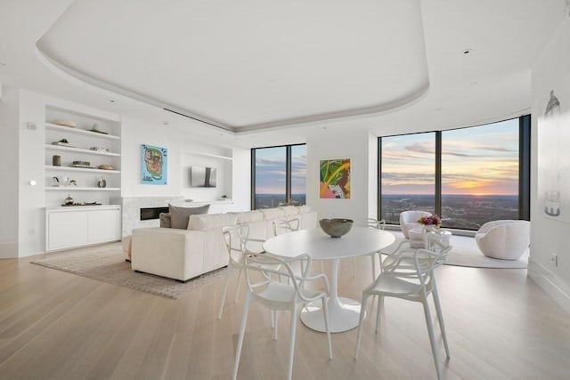 dining room with a raised ceiling, a wealth of natural light, light wood finished floors, and built in shelves