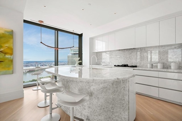 kitchen featuring a wall of windows, decorative backsplash, a sink, light wood finished floors, and white cabinets