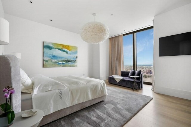 bedroom featuring floor to ceiling windows, baseboards, and wood finished floors