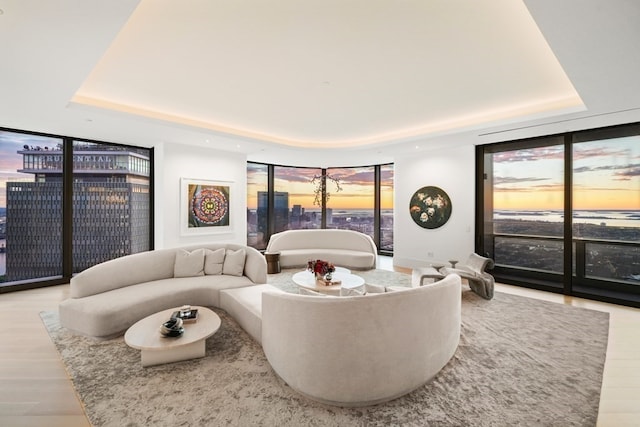 living room featuring floor to ceiling windows, a water view, light wood-type flooring, and a tray ceiling