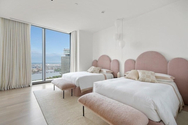 bedroom featuring a water view, floor to ceiling windows, wood finished floors, and a view of city