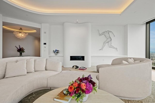 living area with a tray ceiling and a glass covered fireplace