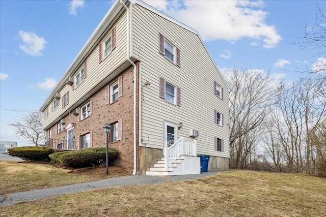 view of property exterior featuring a wall unit AC, a yard, and brick siding