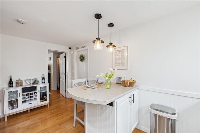 kitchen with decorative light fixtures, a breakfast bar, light countertops, light wood-style flooring, and a peninsula