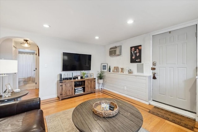 living room featuring recessed lighting, arched walkways, an AC wall unit, and wood finished floors