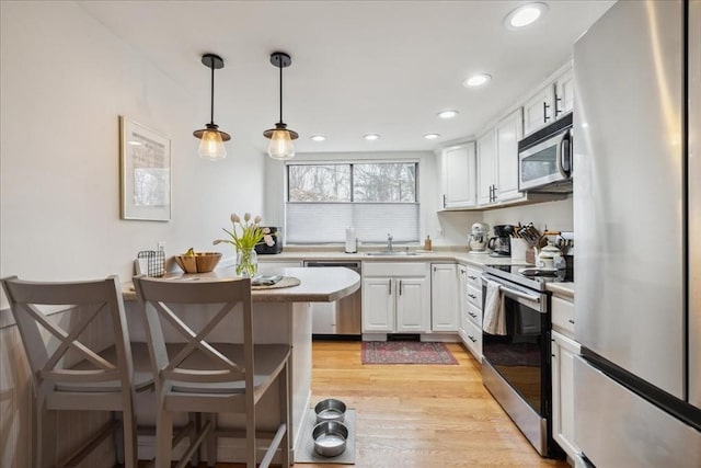 kitchen with a sink, light countertops, white cabinets, light wood-style floors, and appliances with stainless steel finishes