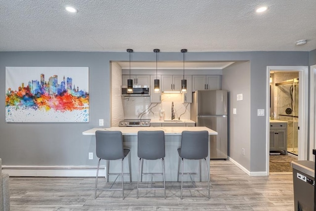 kitchen featuring a baseboard radiator, stainless steel appliances, a breakfast bar, light wood-style floors, and light countertops