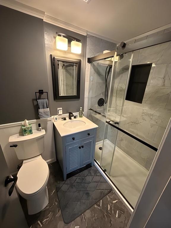 bathroom with toilet, marble finish floor, crown molding, vanity, and a shower stall