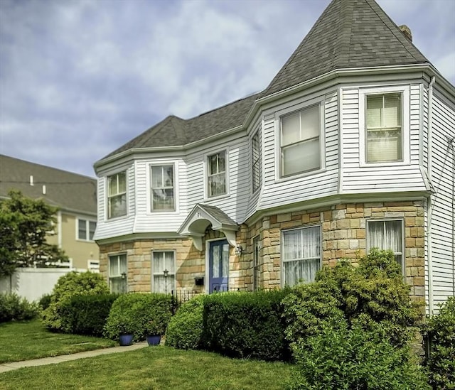 victorian home featuring stone siding and a front yard