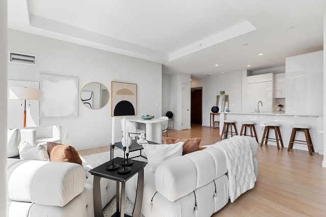 living room featuring sink, light wood-type flooring, and a tray ceiling