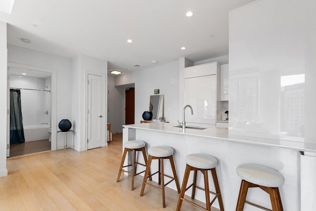 kitchen with a breakfast bar, kitchen peninsula, sink, white cabinetry, and light wood-type flooring