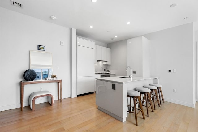 kitchen featuring a breakfast bar area, sink, light wood-type flooring, and white cabinetry