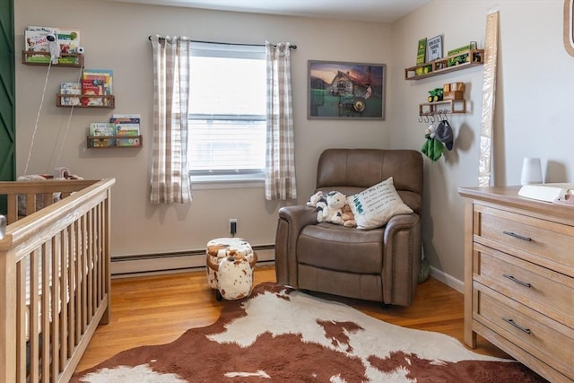 bedroom with a baseboard heating unit, light hardwood / wood-style floors, and a nursery area