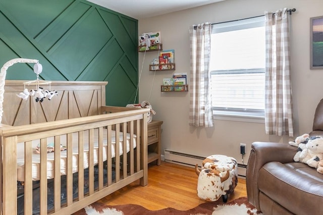 bedroom featuring a crib, a baseboard heating unit, and hardwood / wood-style floors