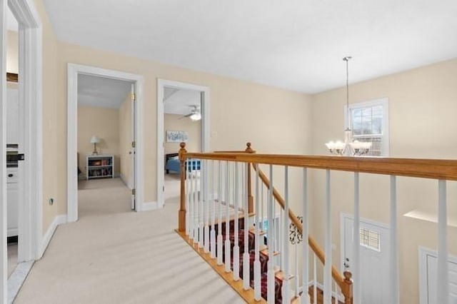 hall featuring baseboards, light carpet, an upstairs landing, and a chandelier
