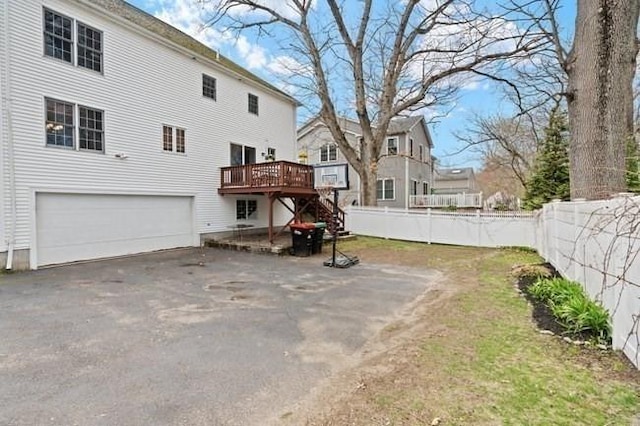 rear view of property with driveway, a wooden deck, stairway, fence, and an attached garage