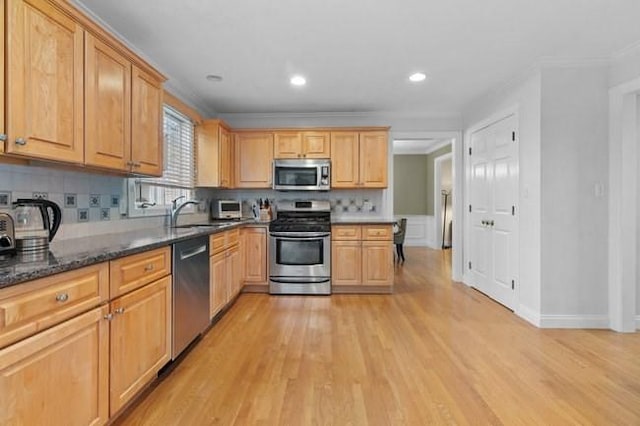 kitchen featuring crown molding, a sink, light wood-style floors, stainless steel appliances, and tasteful backsplash