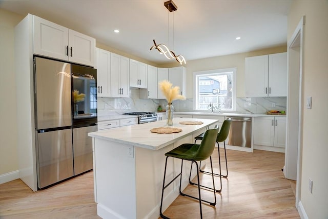 kitchen featuring tasteful backsplash, light wood finished floors, appliances with stainless steel finishes, a kitchen breakfast bar, and white cabinets