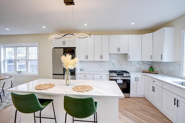 kitchen featuring a kitchen breakfast bar, light stone countertops, appliances with stainless steel finishes, and white cabinetry