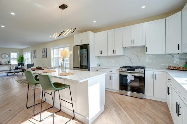 kitchen featuring light wood finished floors, backsplash, appliances with stainless steel finishes, and a center island