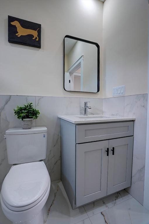 half bath featuring a wainscoted wall, marble finish floor, toilet, and vanity