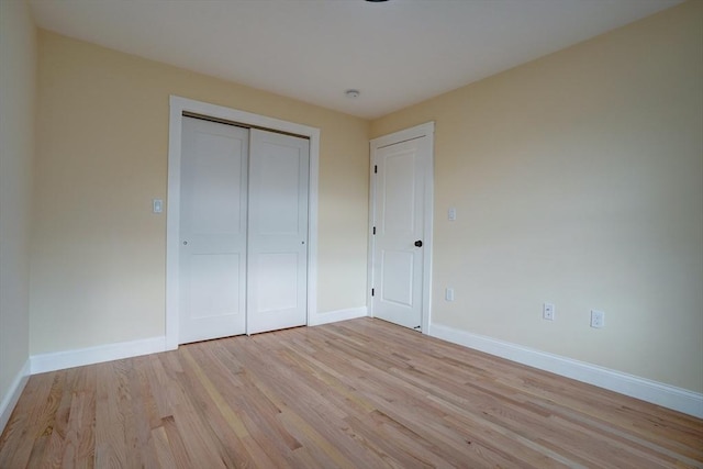 unfurnished bedroom featuring light wood-style flooring, baseboards, and a closet