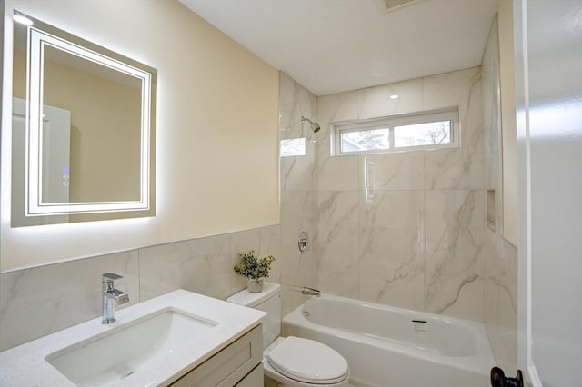 bathroom with tile walls, a wainscoted wall, toilet, vanity, and  shower combination