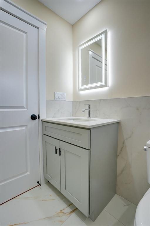 bathroom with a wainscoted wall, toilet, marble finish floor, tile walls, and vanity