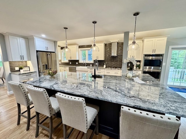 kitchen featuring stainless steel appliances, tasteful backsplash, a spacious island, white cabinetry, and wall chimney exhaust hood