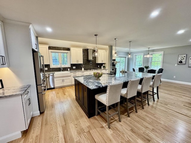 kitchen with a sink, appliances with stainless steel finishes, a breakfast bar, light wood finished floors, and a large island