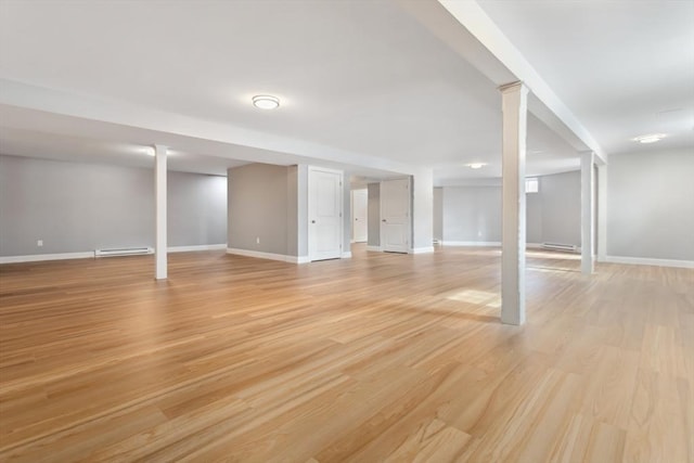 finished basement with a baseboard heating unit, baseboards, and light wood-type flooring