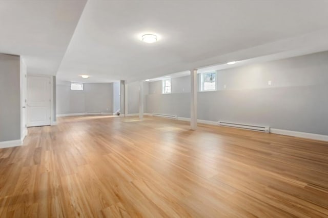 basement with a baseboard heating unit, light wood-style flooring, and baseboards