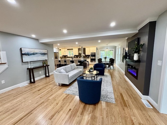 living room with light wood-style floors, baseboards, ornamental molding, and recessed lighting
