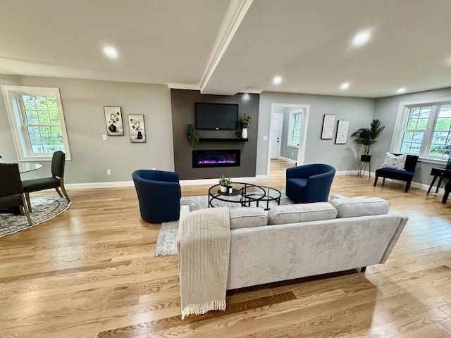 living area with a glass covered fireplace, baseboards, plenty of natural light, recessed lighting, and light wood-type flooring