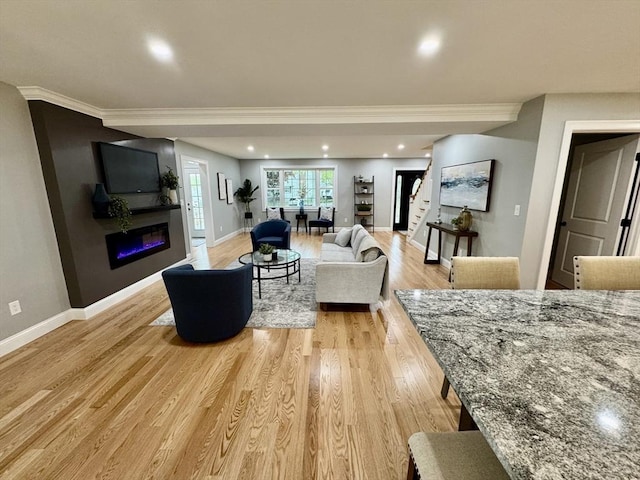 living area featuring stairs, ornamental molding, a glass covered fireplace, baseboards, and light wood-style flooring