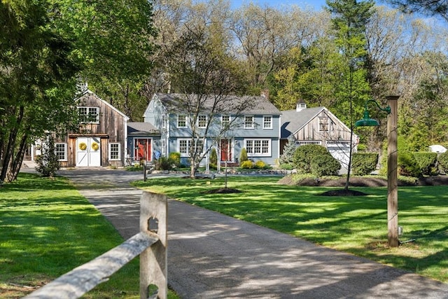 shingle-style home featuring a chimney, driveway, and a front lawn