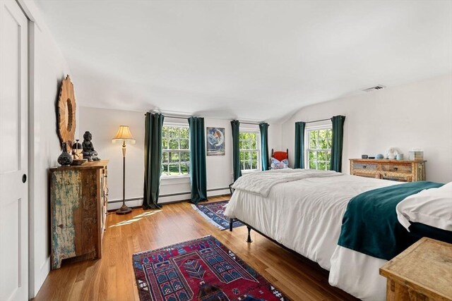 bedroom featuring visible vents, a baseboard radiator, lofted ceiling, and light wood-type flooring