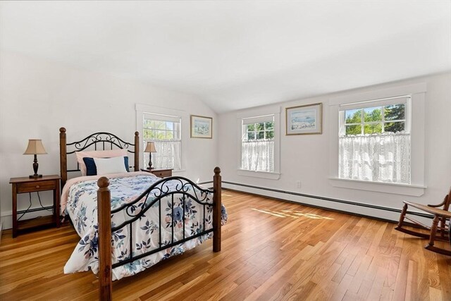 bedroom featuring light wood-style flooring, a baseboard heating unit, and vaulted ceiling